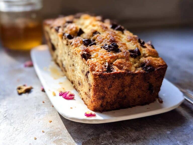 A freshly baked loaf of Banana Bread Ricotta studded with chocolate chips, sitting on a white platter.
