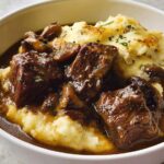 Close-up of tender chunks of Beef Stew With Onion Gravy served over creamy mashed potatoes.