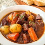 Close-up of a rich Beef Stew With Potatoes, tender beef chunks, and carrots in a white bowl, garnished with parsley.