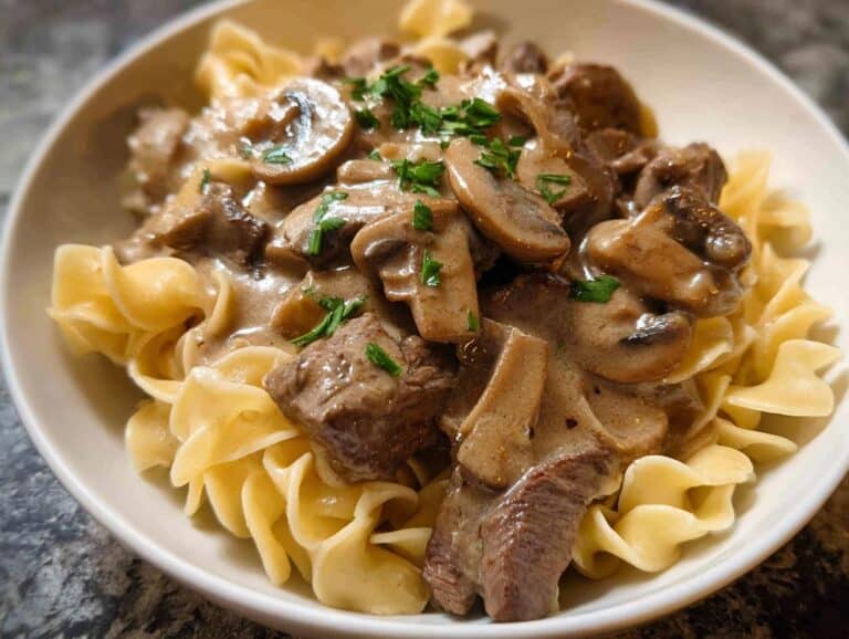 Close-up of a creamy Beef Stroganoff Dinner with sliced mushrooms and beef chunks over wide egg noodles.