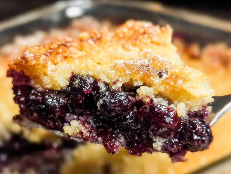 Close-up of a fork lifting a warm, gooey serving of Blueberry Dump Cake showing the rich blueberry filling and golden topping.
