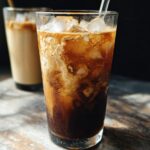 Close-up of a tall glass filled with ice, dark coffee, and swirling oatmilk for a Brown Sugar Oatmilk Shaken Espresso.