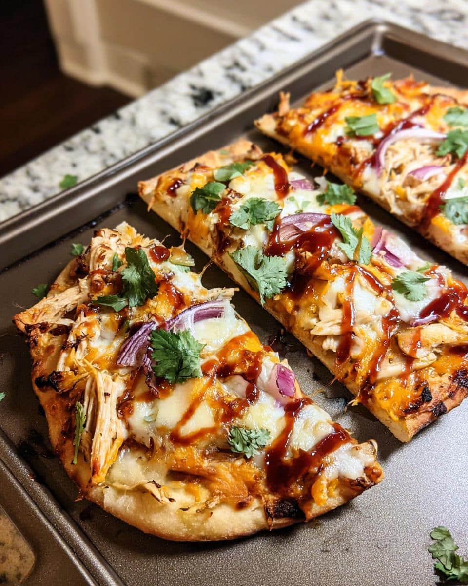 Three slices of Cheesy Chicken Flatbread Pizza topped with BBQ sauce, red onion, and cilantro on a dark baking sheet.