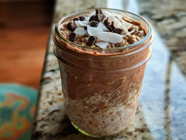 Close-up of Chocolate Coconut Overnight Oats layered in a mason jar, topped with coconut flakes and chocolate chips.
