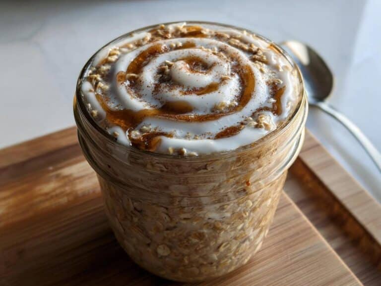 Close-up of Cinnamon Roll Overnight Oats in a mason jar topped with white icing swirled with caramel and cinnamon.