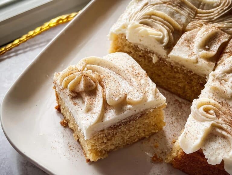 Close-up of a square slice of Cinnamon Sugar Snack Cake topped with creamy white frosting and a dusting of cinnamon.