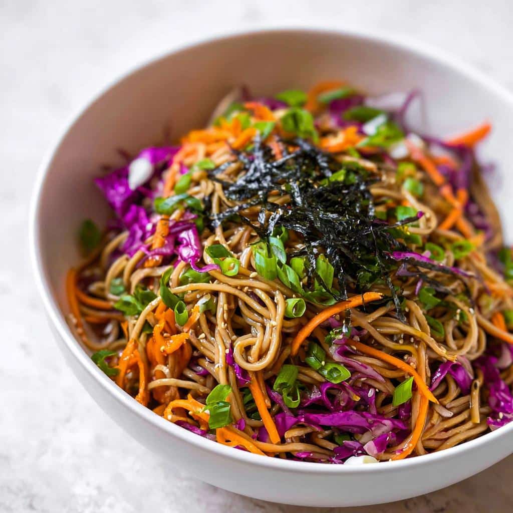 Close-up of a colorful Cold Soba Noodle Lunch Bowl topped with shredded carrots, purple cabbage, scallions, and nori.