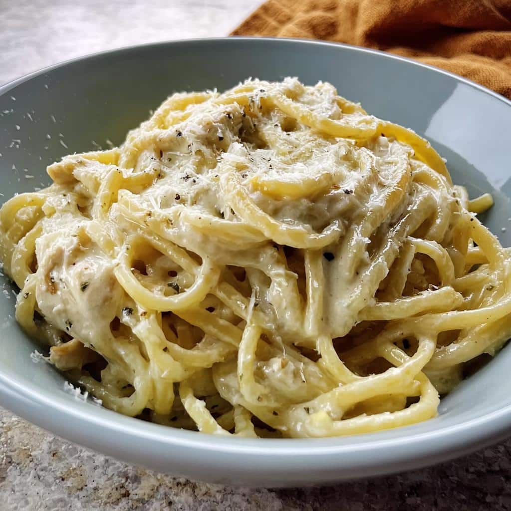 Close-up of rich Creamy Garlic Chicken Pasta coated in a thick white sauce and topped with grated Parmesan cheese.