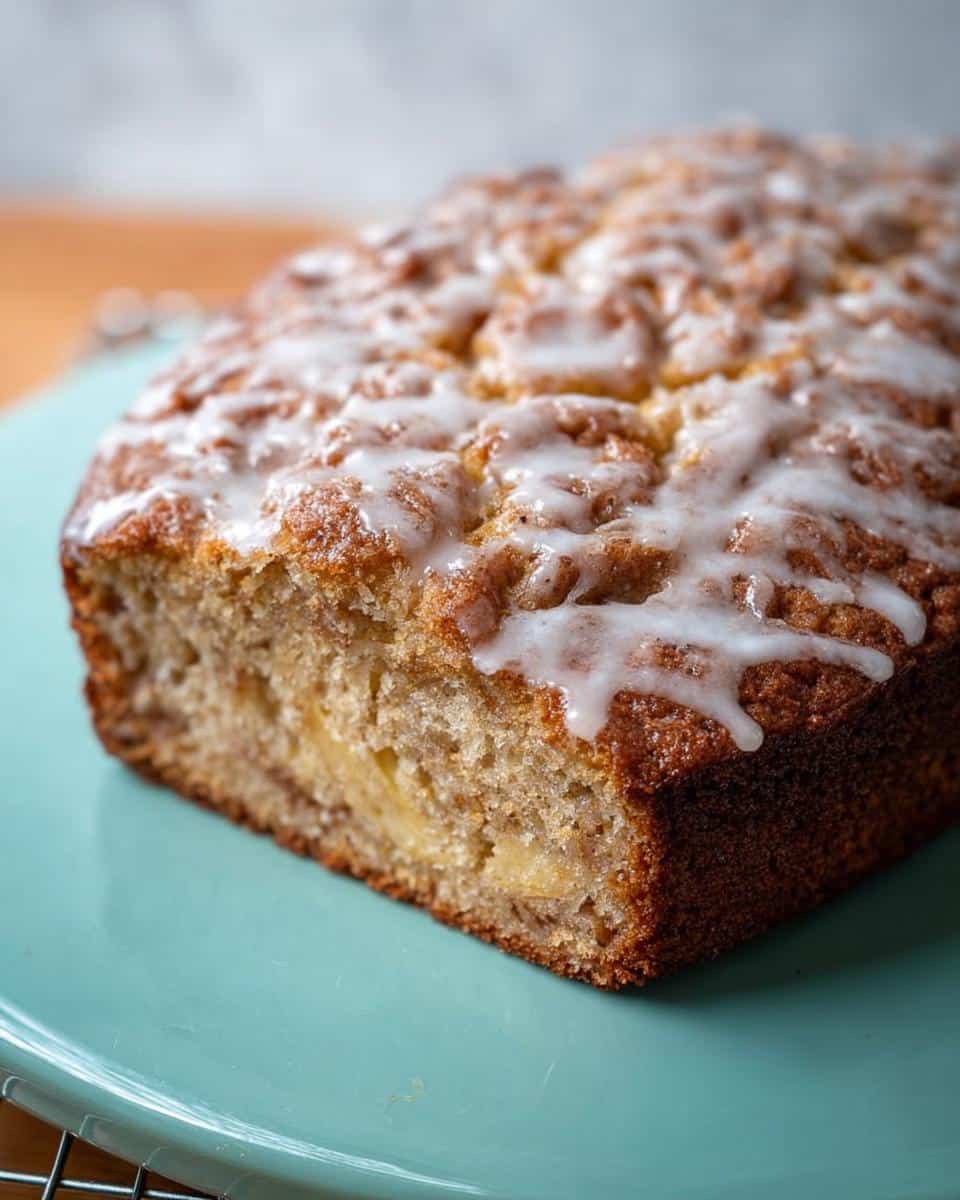 Close-up of a freshly baked Easy Apple Cinnamon Cake loaf with a white glaze drizzled over the top.