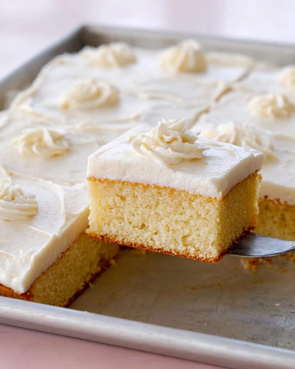 A slice of moist Easy Vanilla Sheet Cake being lifted from the pan with white frosting.