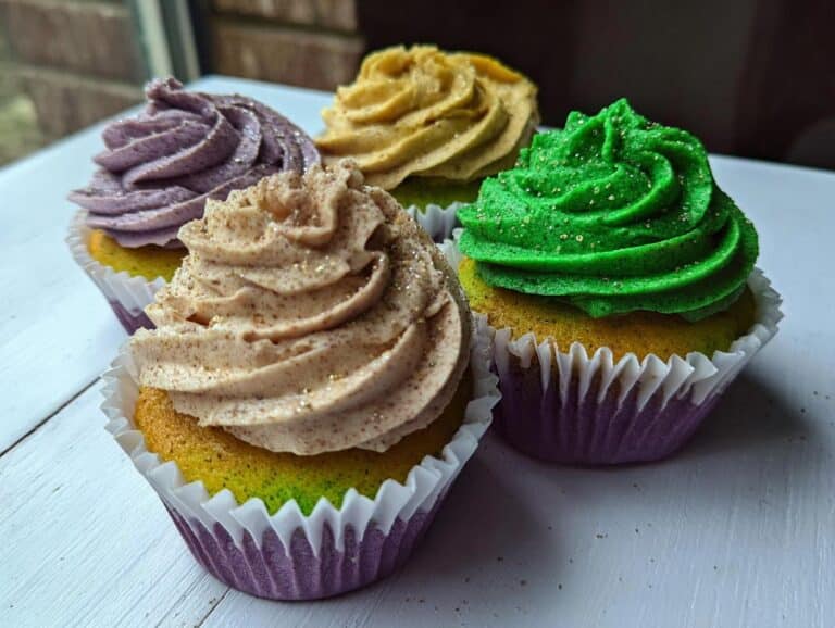 Four Fat Tuesday Dessert cupcakes featuring purple, gold, tan, and green frosting with edible glitter.