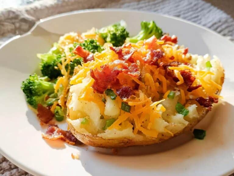 A baked potato half stuffed with cheese, bacon bits, and chives, served alongside steamed broccoli, representing the Loaded Potato Bake.