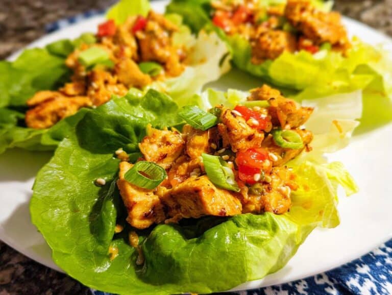 Close-up of a serving of Low Carb Chicken Lettuce Wraps filled with seasoned chicken, topped with green onions and sesame seeds.