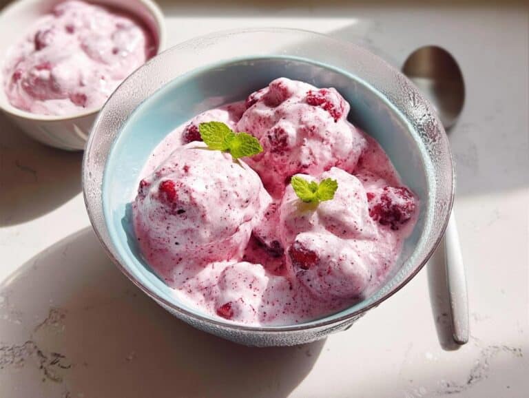 Close-up of three scoops of pink Frozen Fruit Whip in a light blue bowl, garnished with fresh mint leaves.