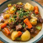 Close-up of a bowl filled with rich Garlic Herb Beef Stew featuring chunks of beef, potatoes, carrots, and celery.
