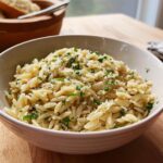 A white bowl filled with creamy Garlic Parmesan Orzo, topped with grated cheese and fresh chopped parsley.