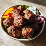 A bowl filled with perfectly browned Gluten Free Air Fryer Meatballs served over lettuce with peppers, onion, and tzatziki.