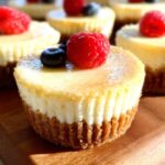 A close-up of several Gluten Free Cheesecake Cups topped with a raspberry and a blueberry, sitting on a wooden board.