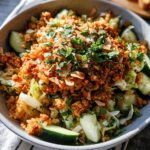 Close-up of a Gluten Free Crispy Rice Bowl topped with savory crumbles, sliced cucumbers, and fresh herbs.