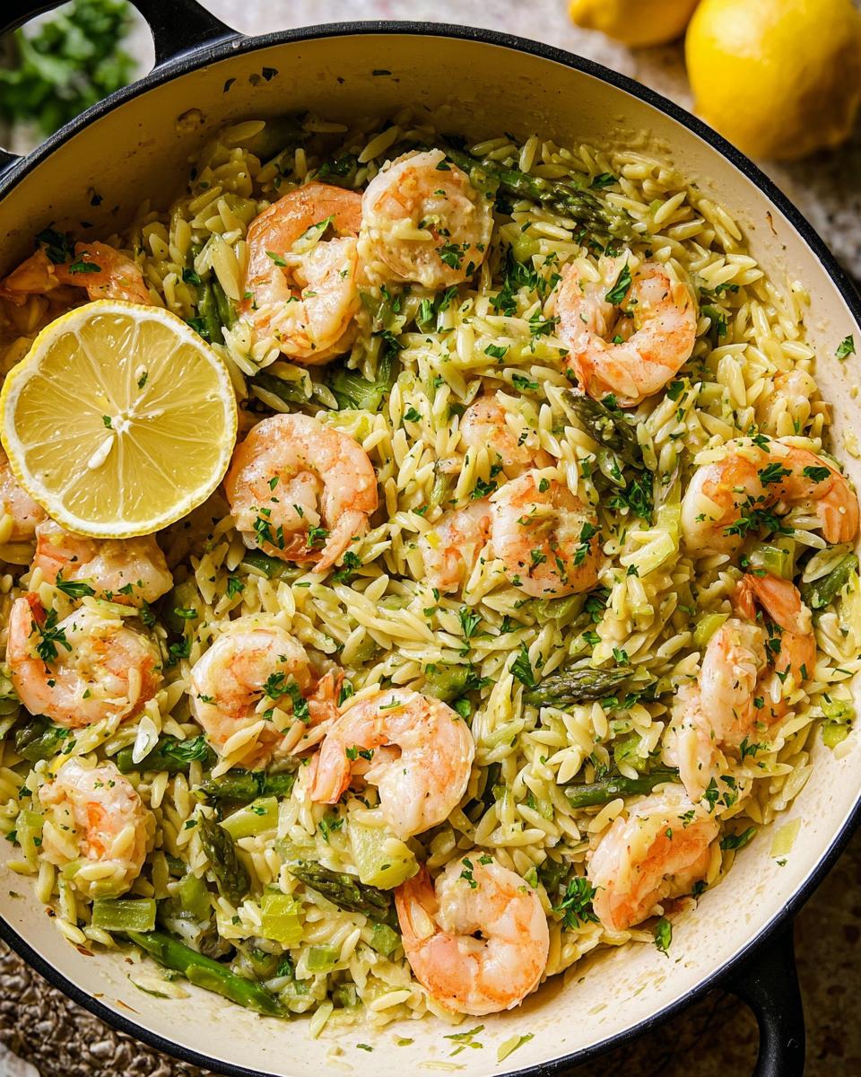 Overhead view of Gluten Free Lemon Orzo with Shrimp, asparagus, and a lemon slice in a skillet.
