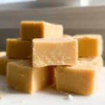 A stack of creamy, light brown squares of Gluten Free Peanut Butter Fudge resting on a white surface.