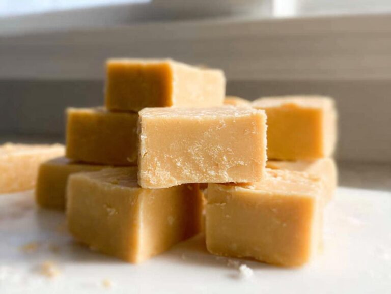 A stack of creamy, light brown squares of Gluten Free Peanut Butter Fudge resting on a white surface.