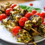 Close-up of grilled Gluten Free Pesto Chicken Skewers alternating with roasted cherry tomatoes on a white plate.