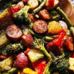 Close-up of roasted sausage slices, potatoes, broccoli, and peppers in a Gluten Free Sheet Pan Sausage Veggies dish.