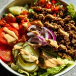 Close-up of a Gluten Free Smash Burger Bowl featuring seasoned ground beef, lettuce, tomatoes, pickles, and sauce.