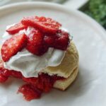 Close-up of a Gluten Free Strawberry Shortcake with macerated strawberries and whipped cream on a white plate.