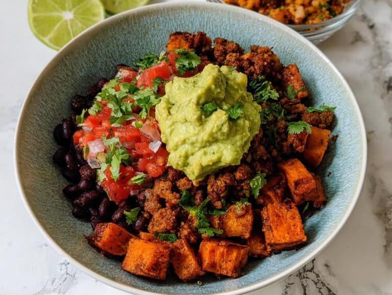 A vibrant bowl of Gluten Free Sweet Potato Taco Bowls topped with seasoned meat, black beans, pico de gallo, and a dollop of guacamole.