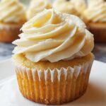 A close-up of one perfectly baked Gluten Free Vanilla Cupcakes topped with swirls of creamy vanilla buttercream frosting.