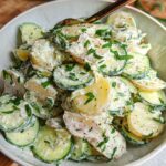 Close-up of a creamy Gluten Free Viral Cucumber Salad featuring sliced potatoes and cucumbers tossed in a white dressing and sprinkled with herbs.