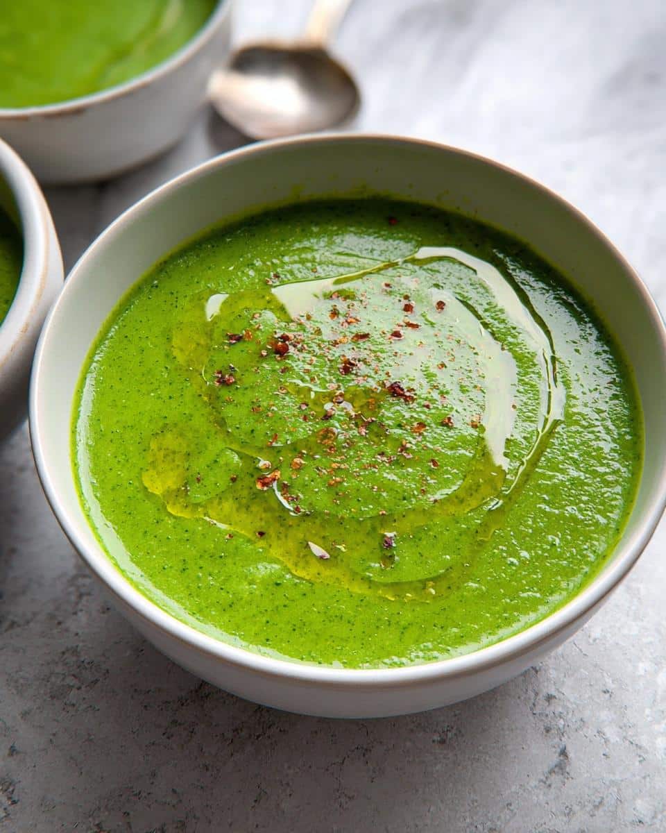 Close-up of a bowl of vibrant Green Detox Soup, drizzled with olive oil and sprinkled with red pepper flakes.