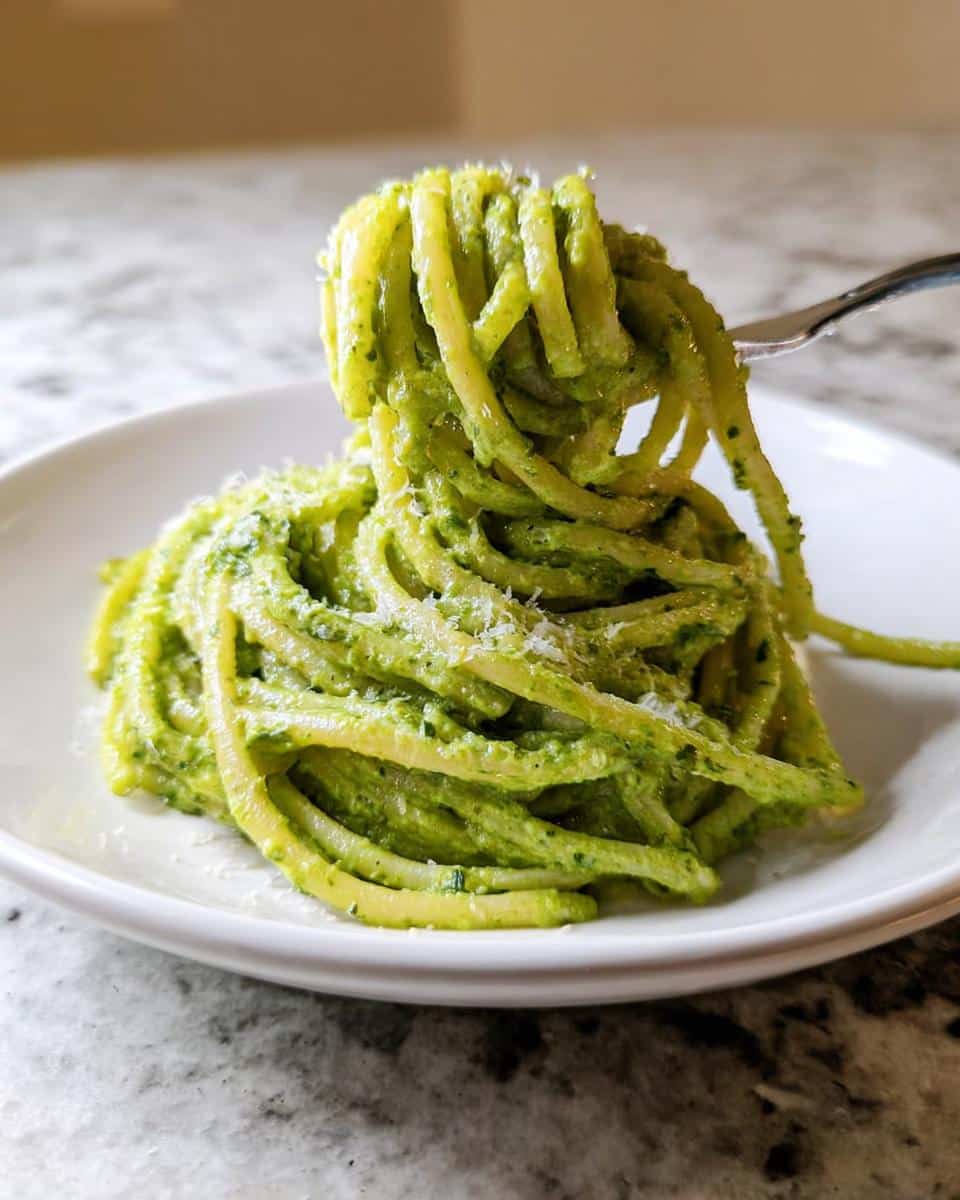 A fork lifts a twirl of vibrant Green Pasta Alfredo coated in creamy sauce and topped with grated Parmesan cheese.