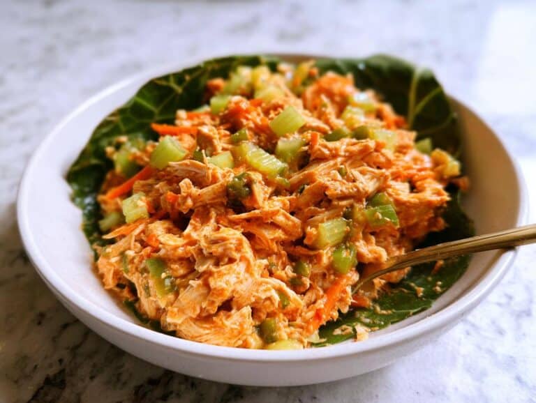 A close-up of a vibrant Low Carb Buffalo Chicken Salad served in a white bowl lined with a large green leaf.