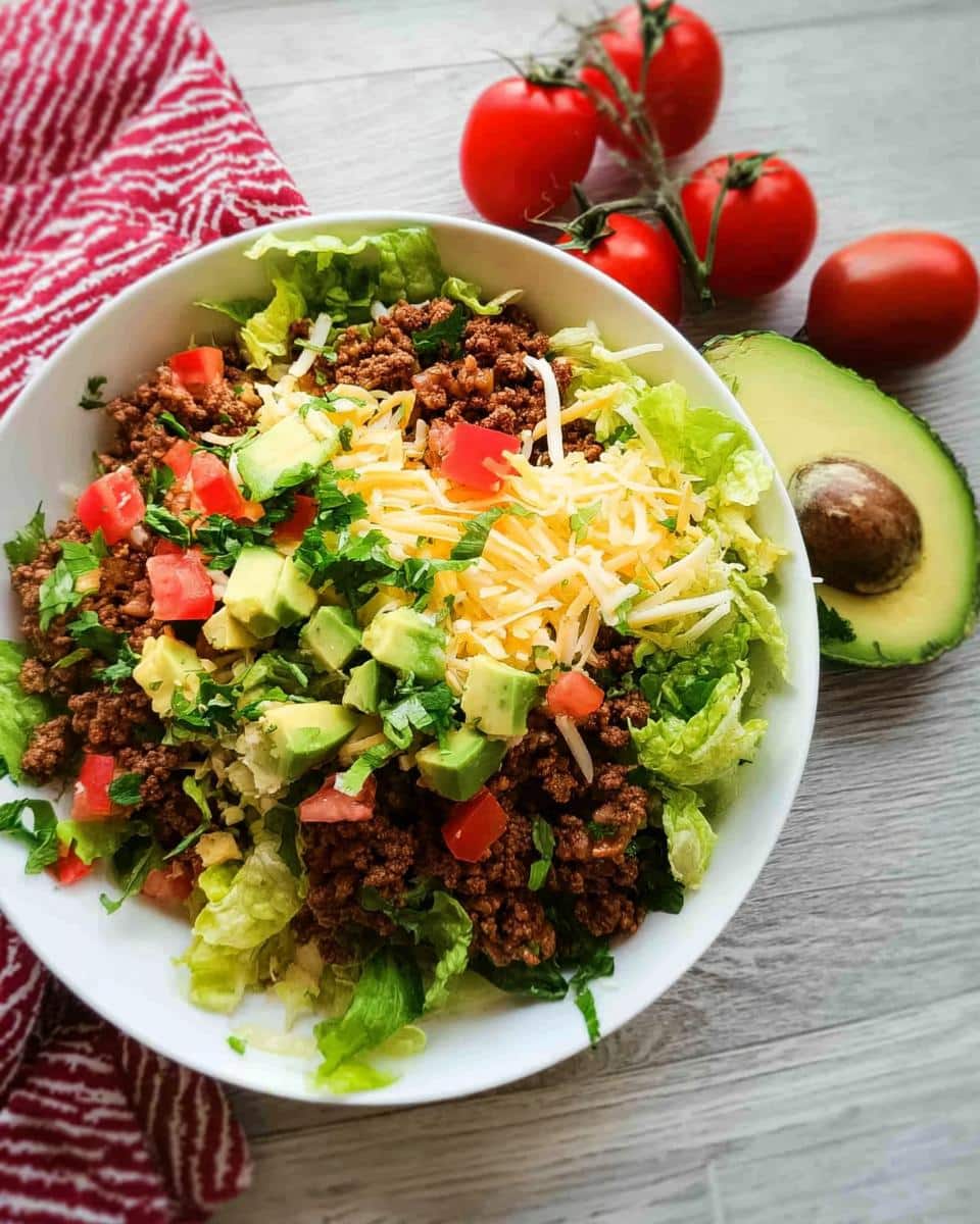 A vibrant bowl of Low Carb Taco Salad featuring seasoned ground beef, lettuce, cheese, avocado, and tomatoes.