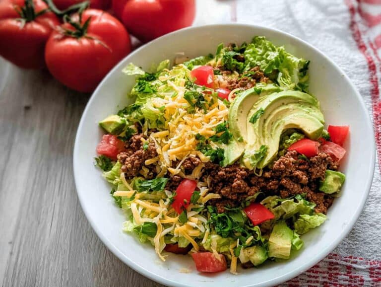 A vibrant bowl of Low Carb Taco Salad featuring seasoned ground beef, shredded cheese, diced tomatoes, and sliced avocado.