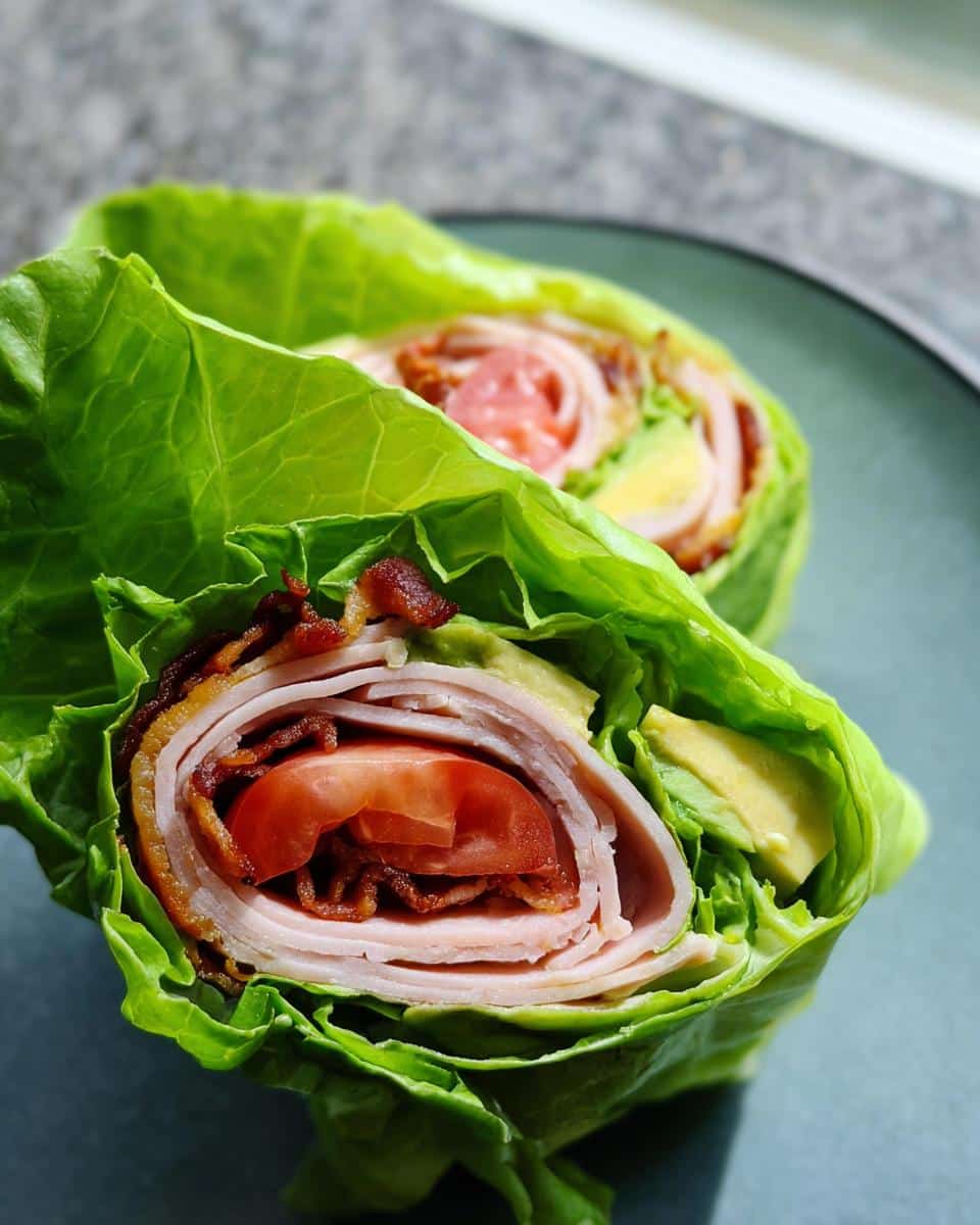 Two halves of Low Carb Turkey Roll Ups wrapped in crisp lettuce, showing turkey, bacon, tomato, and avocado inside.