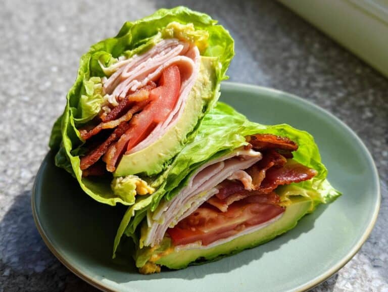 Two halves of Low Carb Turkey Roll Ups filled with turkey, bacon, tomato, and avocado, wrapped tightly in crisp lettuce leaves.