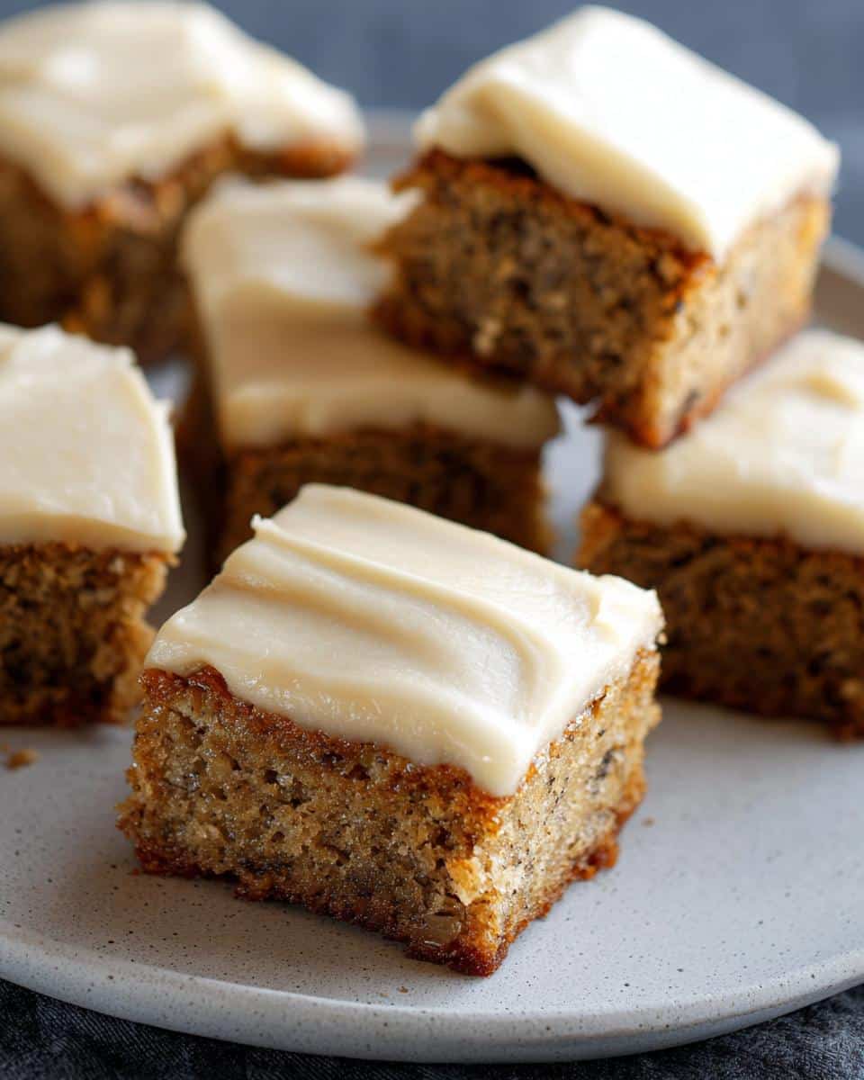 Close-up of a frosted square of moist Banana Bread Bars on a light gray plate.