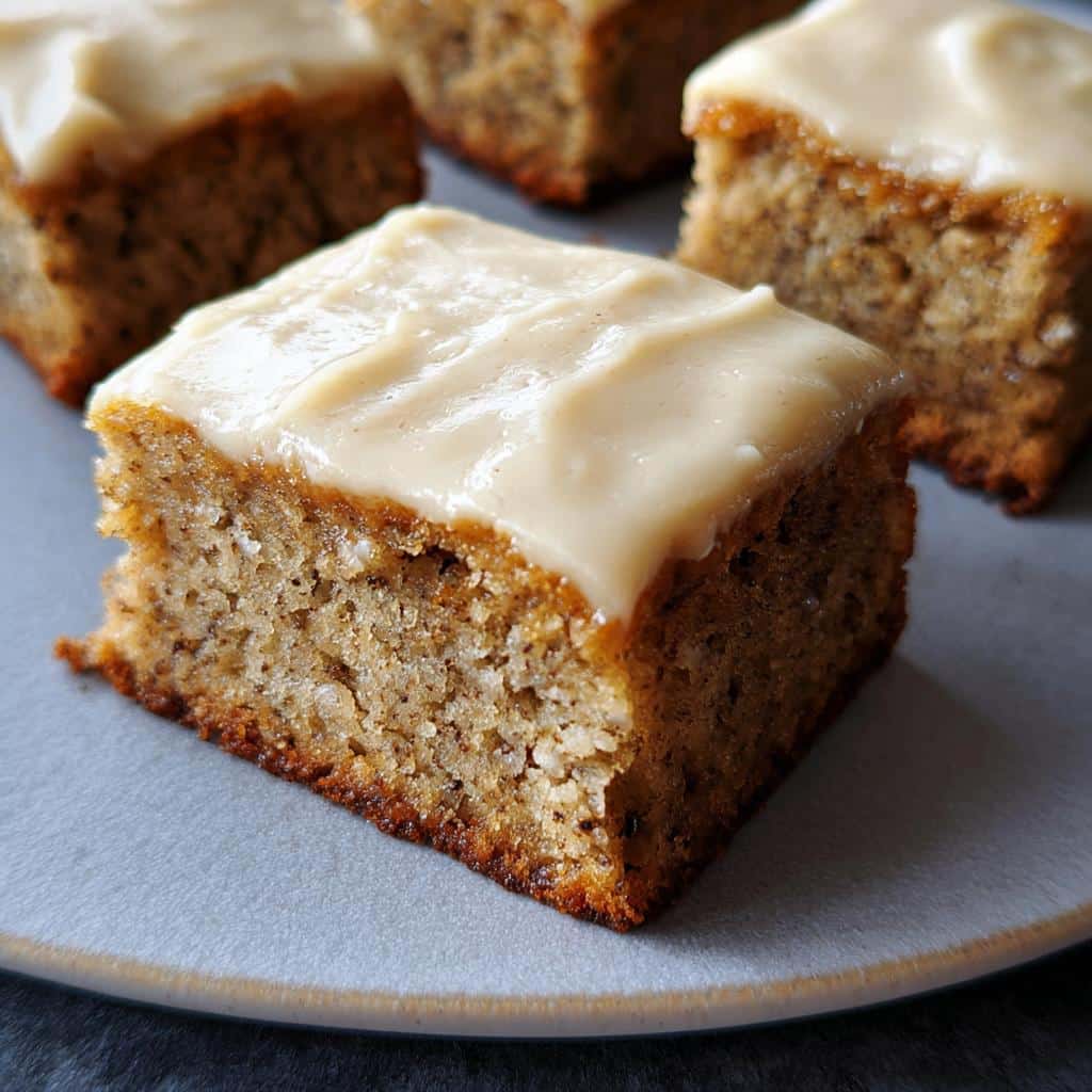 Close-up of a square slice of moist Banana Bread Bars topped with thick, creamy frosting on a plate.