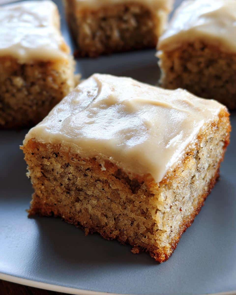Close-up of a square Banana Bread Bars slice topped with thick, creamy frosting on a grey plate.