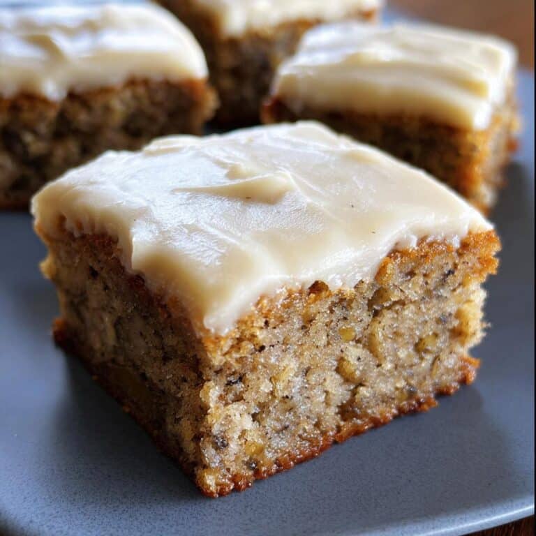 Close-up of a square Banana Bread Bars slice topped with thick, creamy frosting on a blue plate.