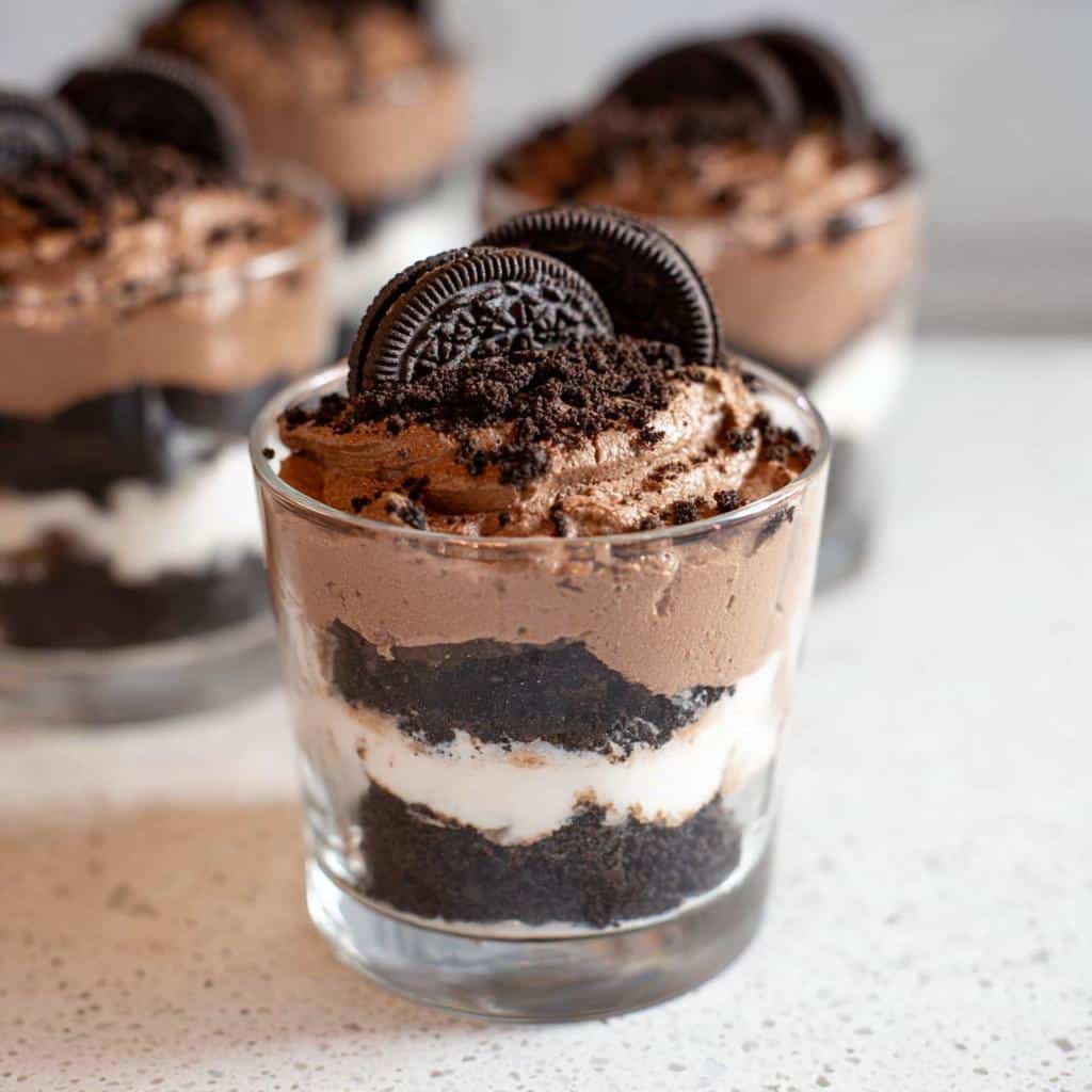 A close-up of one of the No-Bake Oreo Dessert Cups, layered with chocolate mousse, cream, and Oreo crumbs, topped with a whole Oreo.