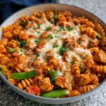 Close-up of cheesy One Pan Chicken Pasta with chicken chunks, rotini pasta, and green vegetables in a skillet.