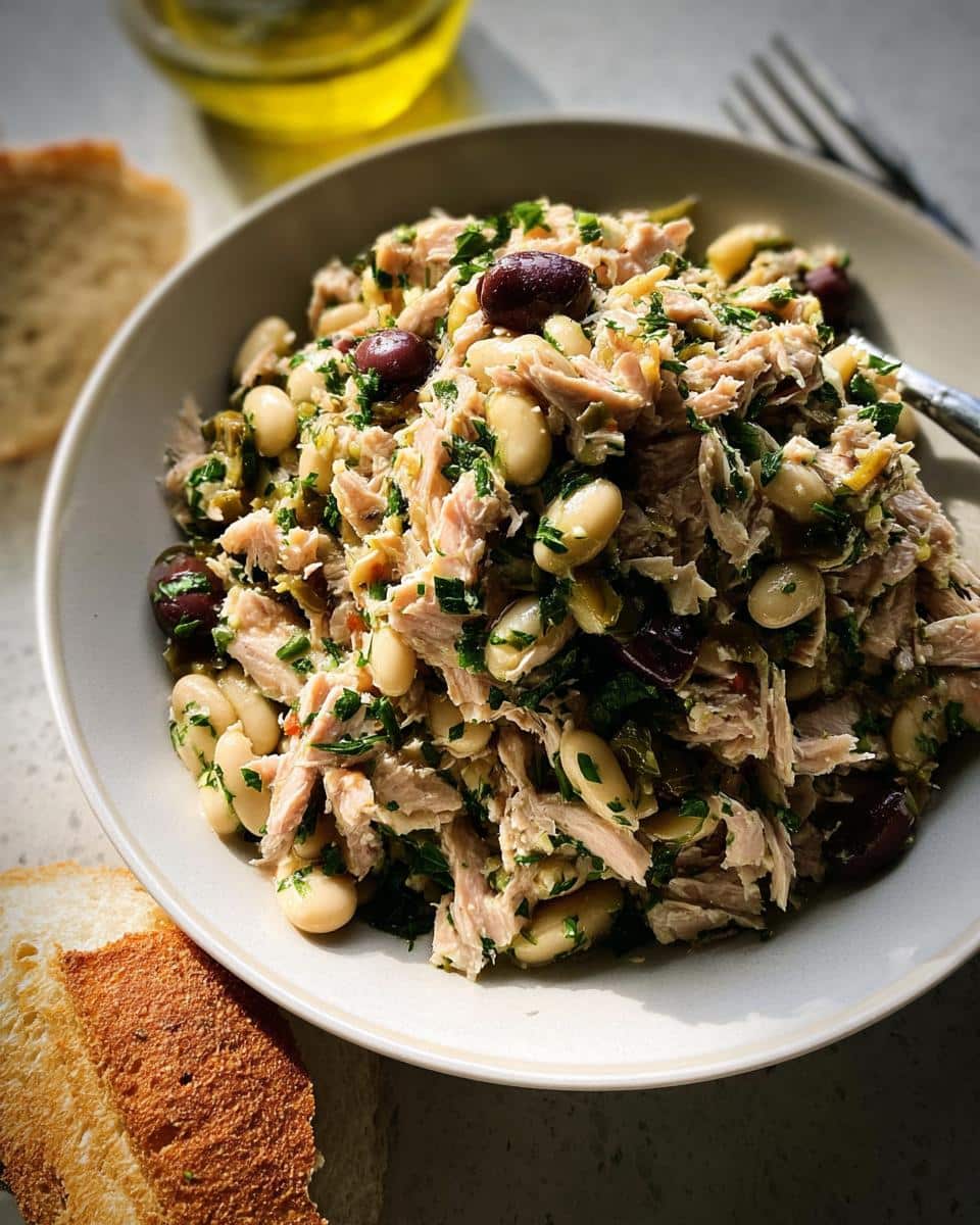 A close-up of a hearty Tuna White Bean Lunch Salad mixed with white beans and olives, served with toasted bread.