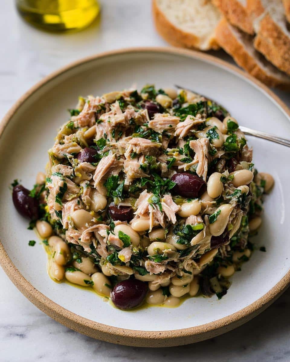 A molded serving of Tuna White Bean Lunch Salad featuring tuna, cannellini beans, parsley, and Kalamata olives, drizzled with oil.