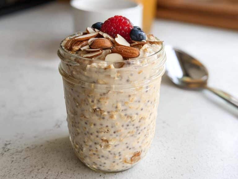 A jar of creamy Vanilla Almond Overnight Oats topped with sliced almonds, a raspberry, and blueberries.