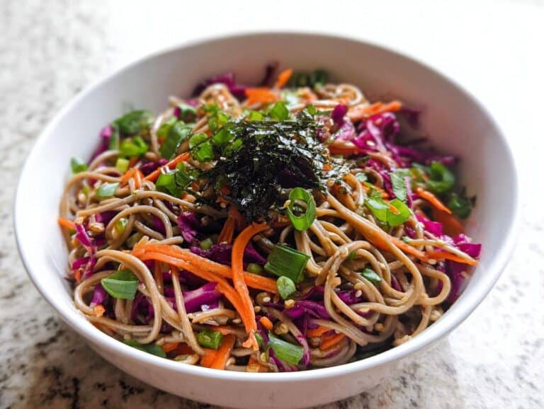 A close-up of a vibrant Cold Soba Noodle Lunch Bowl topped with shredded carrots, red cabbage, and nori.